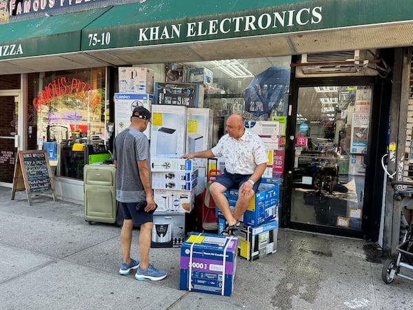 Mudassar Khan, right, talks with a customer while sitting outside his electronics store with air conditioners and fans for sale on display, Tuesday, June 24, 2025, in New York. (AP Photo/Cedar Attanasio)
