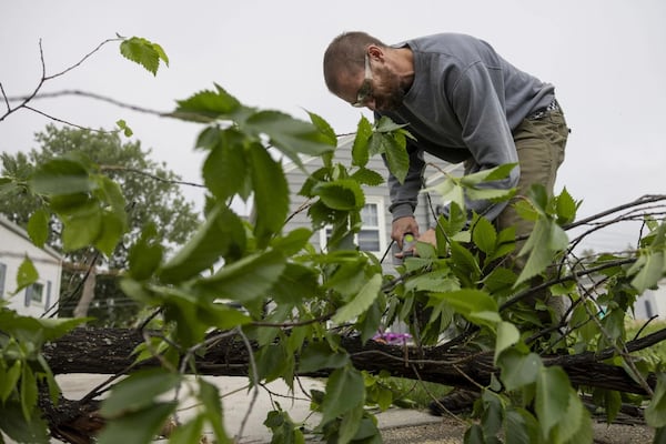 Casey Fiest uses an electric chainsaw to cut limbs off of a broken tree laying in a yard from the previous night's severe thunderstorms in Bismarck, N.D., on Saturday, June 21, 2025. (Tanner Ecker /The Bismarck Tribune via AP)