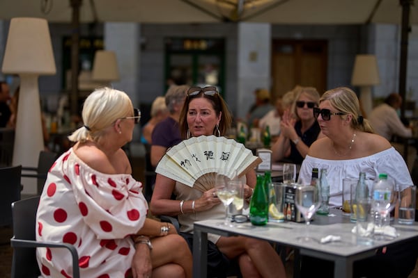 A woman cools herself with a hand fan at a restaurant terrace during a heat wave in Madrid, Spain, Tuesday, July 1, 2025. (AP Photo/Manu Fernandez)