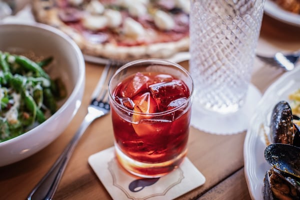 A negroni cocktail surrounded by food items on a restaurant table.