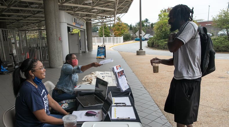 DeKalb County election officials Nytia Harris, from left, and Lamashia Davis work to spread information and share a voter registration application with Christoper Brooks at the Chamblee MARTA station. (Jenni Girtman for The Atlanta Journal-Constitution)