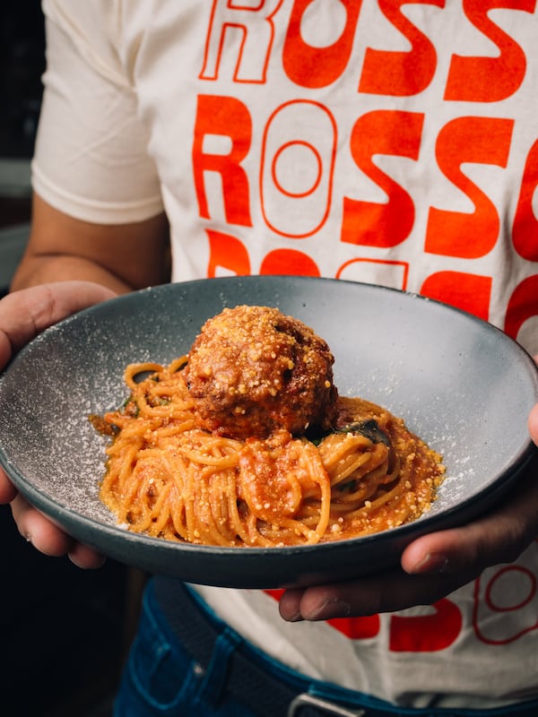 A man holds a plate of spaghetti topped with a single, large meatball