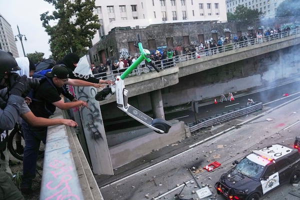 A protester throws a scooter at a police vehical near the metropolitan detention center of downtown Los Angeles, Sunday, June 8, 2025, following last night's immigration raid protest. (AP Photo/Jae C. Hong)