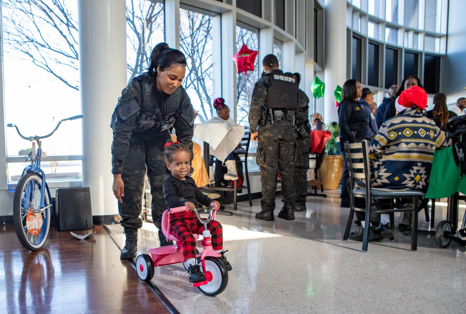 DeKalb County Sheriff’s Office holds the 16th annual Adopt-A-Family celebration on Tuesday, Dec 16, 2023 where Officer Davis, left, helps 3-year old Olivia Banks with her new bike. Law enforcement officers donate their own money and buy gifts for about a dozen local children.  (Jenni Girtman for The Atlanta Journal-Constitution)