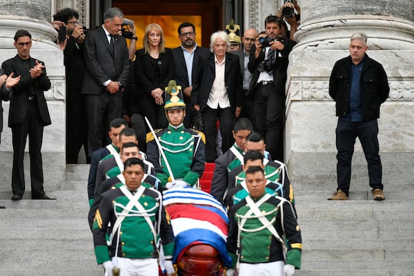 Uruguay's President Yamandu Orsi, back left, his wife Laura Alonsoperez, second from left, and Lucia Topolansky, the widow of late former President Jose Mujica, watch the honor guard carry his casket after funeral ceremonies at the Legislative Palace in Montevideo, Uruguay, Thursday, May 15, 2025. (AP Photo/Santiago Mazzarovich)