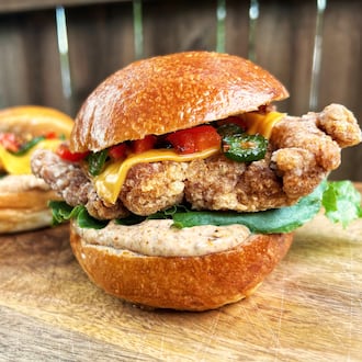 A close look at two large fried chicken sandwiches which are sitting on an outdoor wood table.