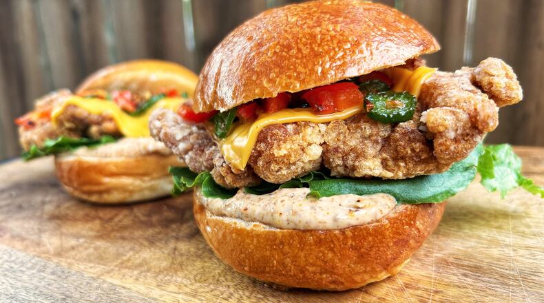 A close look at two large fried chicken sandwiches which are sitting on an outdoor wood table.