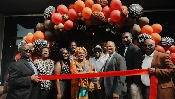 A group of 10 people stands in front of a balloon arch with a ribbon for a ribbon cutting at Ike's Cafe & Grill in Marietta