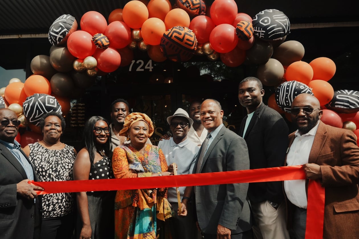 A group of 10 people stands in front of a balloon arch with a ribbon for a ribbon cutting at Ike's Cafe & Grill in Marietta