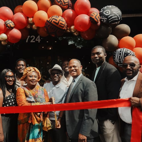A group of 10 people stands in front of a balloon arch with a ribbon for a ribbon cutting at Ike's Cafe & Grill in Marietta