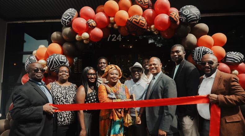 A group of 10 people stands in front of a balloon arch with a ribbon for a ribbon cutting at Ike's Cafe & Grill in Marietta