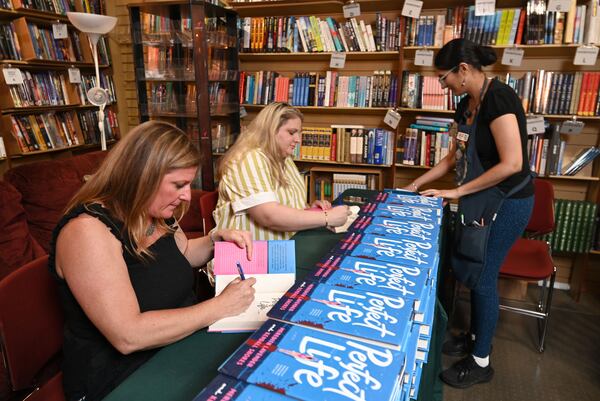 Meredith Lavender, left, and Kendall Shores sign copies of their book, "Perfect Life," with assistance from Preet Singh, right, event coordinator, before an author event at Eagle Eye Book Shop. (Hyosub Shin/AJC)