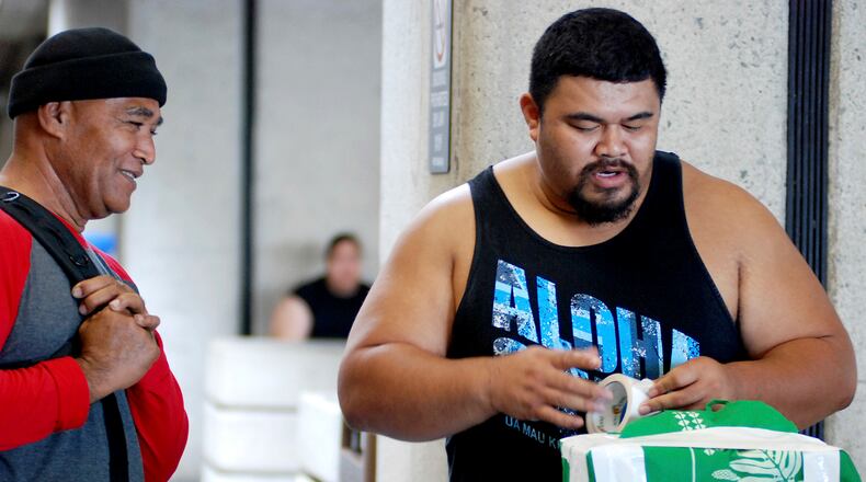 In this Oct. 10, 2016 photo, Mua Migi, left, watches his son Atimua Migi put tape on a carry-on bag before boarding a Hawaiian Airlines flight to Pago Pago, American Samoa at Honolulu International Airport in Honolulu. Atimua Migi doesn't like the airline's new policy of assigning seats at the airport after the airline conducted a survey that involved weighing passengers traveling between Pago Pago and Honolulu. (AP Photo/Jennifer Sinco Kelleher)