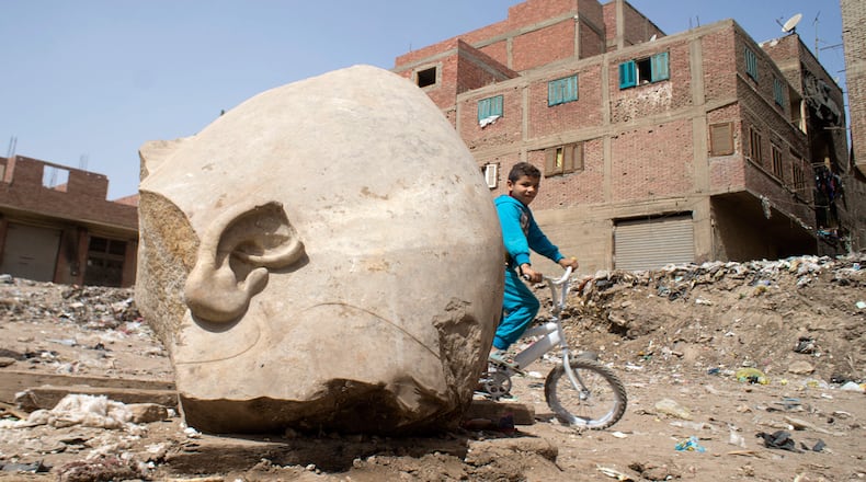 A boy rides his his bicycle past a recently discovered statue in a Cairo slum that may be of pharaoh Ramses II, in Cairo, Egypt, Friday, March 10, 2017. Archeologists in Egypt have discovered a massive statue that may be of pharaoh Ramses II, one of the country's most famous ancient rulers. The colossus, whose head was pulled from mud and groundwater by a bulldozer on Thursday, is around eight meters (yards) tall and was discovered by a German-Egyptian team.