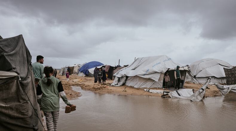Palestinians walk through a flooded area in a temporary tent camp after heavy rainfall in Gaza City, Thursday, March 26, 2026 (AP Photo/Jehad Alshrafi)