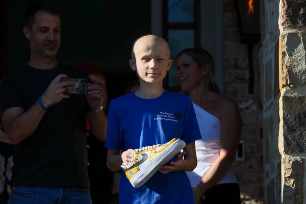 Bowie (holding custom-designed sneakers) and his family watch a parade by the Sandy Springs Police Department that celebrates the trip to the championship game. Also pictured are Burke’s father Ryan (left) and mother Meghan (right). (Jason Getz/AJC)