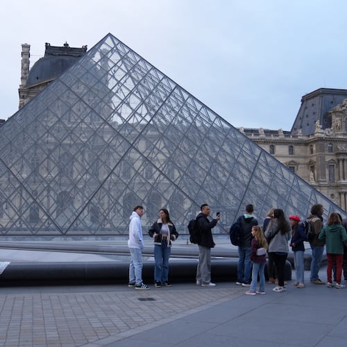 A wedding couple hugs as visitors queue to enter the Louvre museum three days after historic jewels were stolen in a daring daylight heist, Wednesday, Oct. 22, 2025 in Paris. (AP Photo/Thibault Camus)