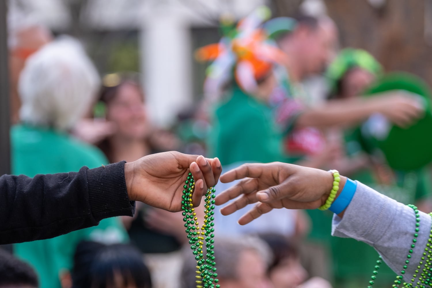 A participant hands beads to a spectator during the Atlanta St. Patrick’s Parade in Midtown on Saturday, March 14, 2026. (Ben Gray for the AJC)