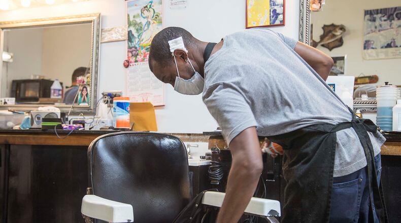 Athens, Georgia  - Wearing a mask, Tony Brown, barber at Brown's Barber Shop, uses a disinfectant wipe to sanitize his chair after servicing a client at the shop in downtown Athens, Friday, April 24, 2020. The family owned small business reopened on Friday, after receiving clearance from Gov. Brian Kemp.  (ALYSSA POINTER / ALYSSA.POINTER@AJC.COM)