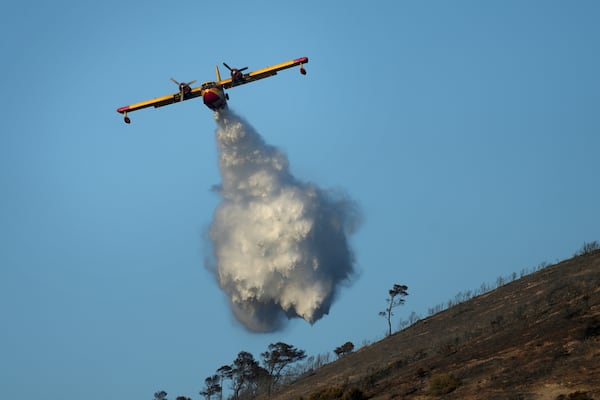 A firefighting airplane sprays water on a hill in Thymari, south of Athens, Thursday, June 26, 2025, as authorities evacuate five locations during Greece's first summer heatwave with temperatures nearing 40 degrees Celsius (104 Fahrenheit). (AP Photo/Thanassis Stavrakis)