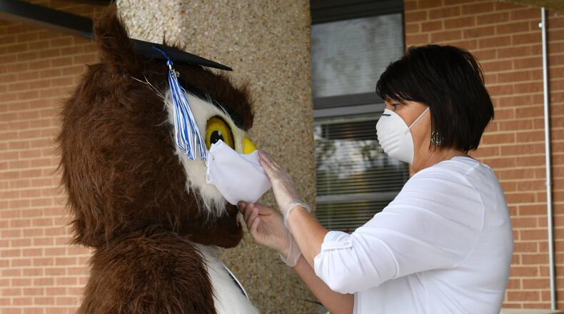 Petra Ordini (right), with office of student services, adjusts a face mask of Gwinnett Online Campus mascot Dr. Whooo, performed by Shannon Williams, as they wait for students picking up their caps and gowns last year outside the main door of Gwinnett Online Campus in Lawrenceville in 2020 .Hyosub Shin/Hyosub.Shin@ajc.com