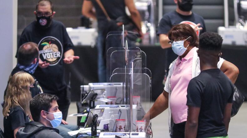 October 12, 2020 Atlanta: People wait to get registered to vote on Monday, Oct. 12, 2020 at State Farm Arena in downtown Atlanta. Eager Georgia voters swarmed to polling places Monday morning, waiting in lines created by high turnout and technical problems at the start of three weeks of early voting before Election Day. A glitch with voter check-in computers held up voters at Georgia’s largest early voting site at State Farm Arena. Lines stopped after voters received an “invalid card” error when inserting green voter access cards into touchscreens. Poll workers had to reboot the arena’s 60 voter check-in tablets and re-import voter information, said Fulton Elections Director Richard Barron. “We apologize to all the voters,” Barron said. (John Spink / John.Spink@ajc.com)