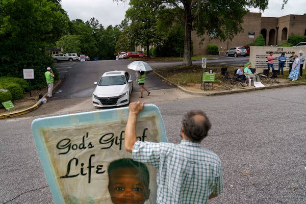 FILE - Anti-abortion protester Steven Lefemine holds a sign as the anti-abortion group, A Moment of Hope, wearing green vests, tries to talk with patients arriving for abortion appointments at Planned Parenthood as a group of Catholics pray off to the side, May 27, 2022, in Columbia, S.C. (AP Photo/David Goldman, File)