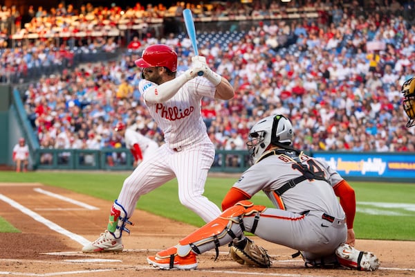 Philadelphia Phillies' Bryce Harper, left, takes an at-bat during the first inning of a baseball game against the San Francisco Giants, Monday, April 14, 2025, in Philadelphia. (AP Photo/Chris Szagola)