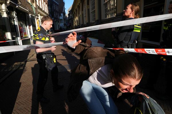 A person walks past police officers and under police tape of a cordoned off area after a stabbing near Dam Square in central Amsterdam, Thursday, March 27, 2025. (AP Photo/Peter Delong)
