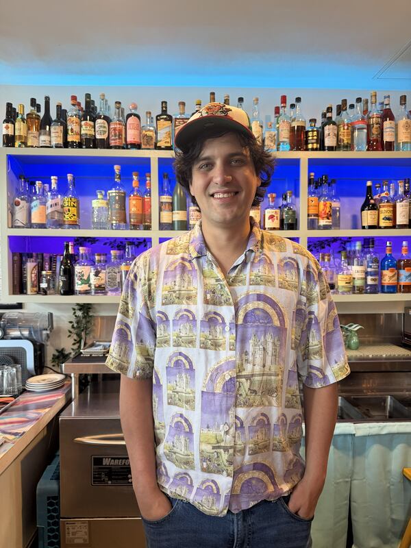 Bartender standing in front of shelves of liquor bottles.