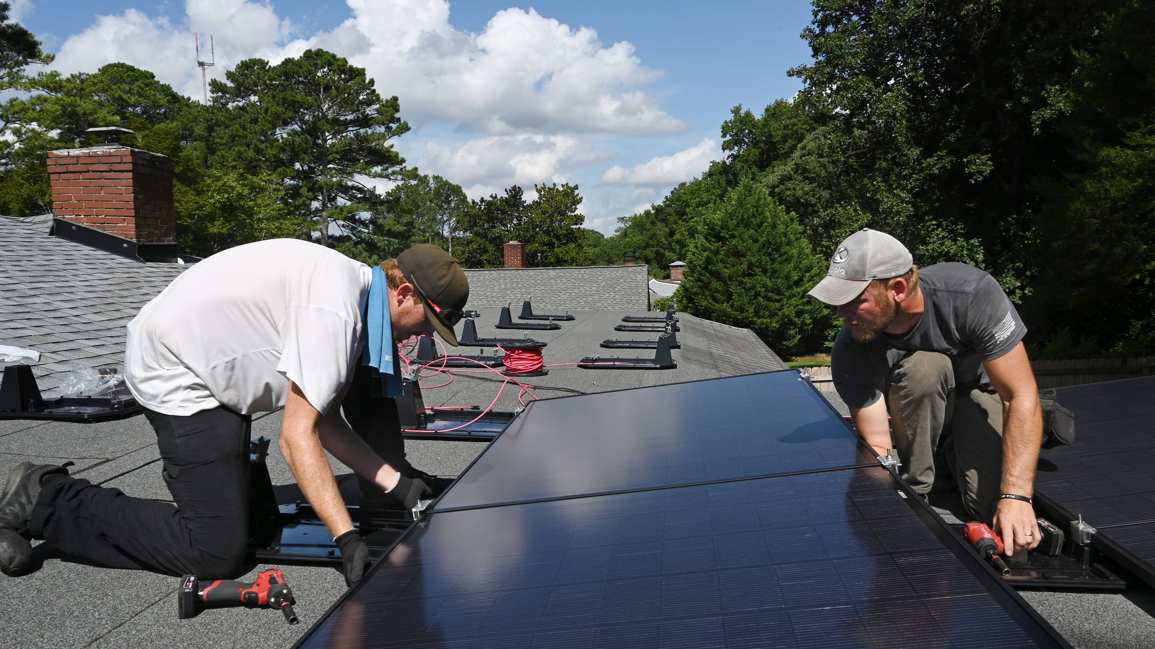 Justin Shelnutt (left) and Ryan Johnson, both with Custom Solar Solutions, install solar panels on the roof of the Adler family home, Thursday, July 17, 2025, in North Druid Hills. Companies like Custom Solar Solutions, who have already been impacted by tariff-driven cost increases, expect to be hit even harder by the reconciliation bill which eliminates a crucial tax incentive.(Hyosub Shin/AJC)