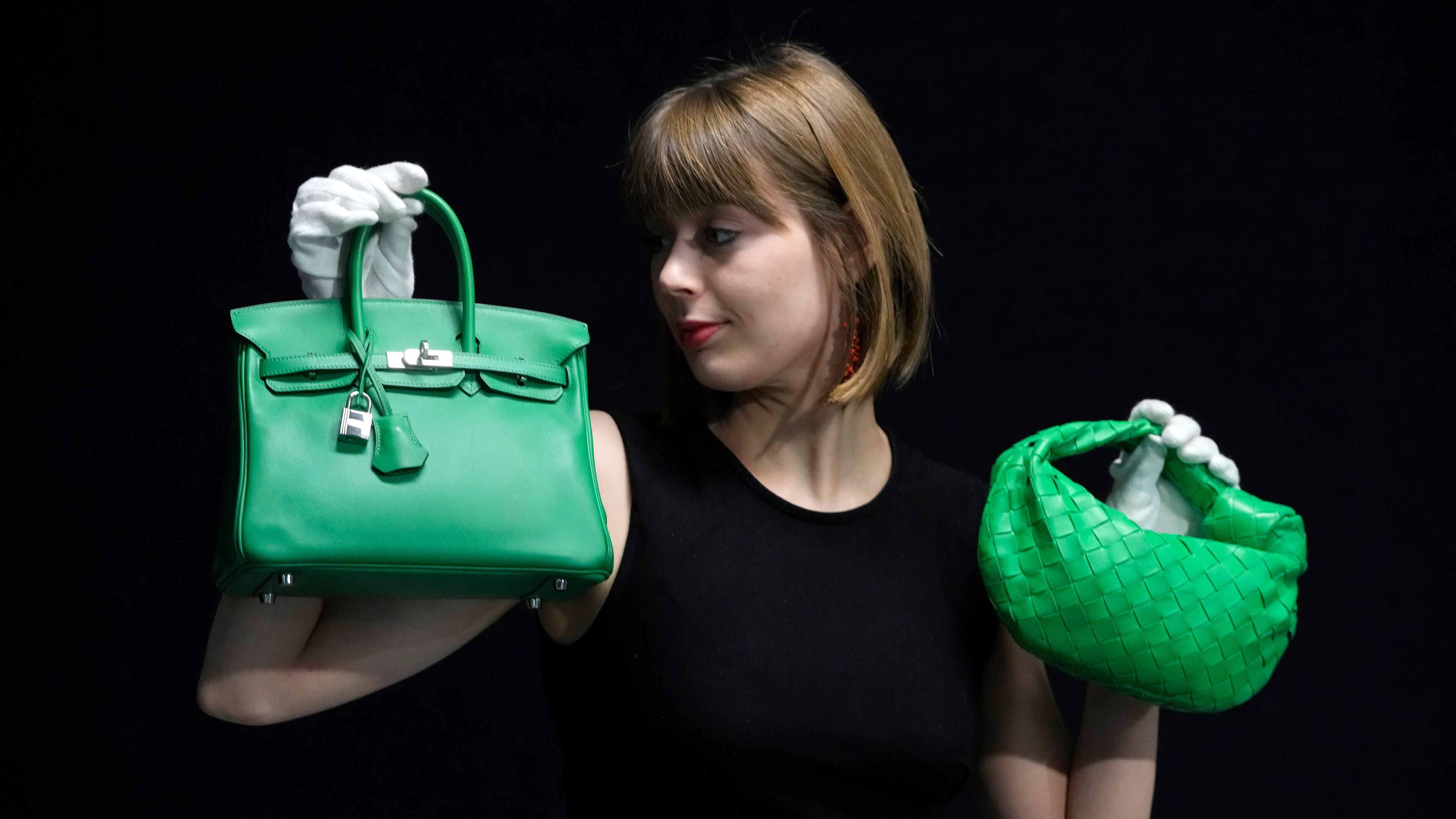 FILE - A Bonhams employee displays a Hermes: a Bambou Swift Leather Birkin 25 bag, left, and a Bottega Veneta: a Parakeet Green Lambskin Mini Jodie, right, at the auction rooms in London on Feb. 26, 2024. (AP Photo/Kirsty Wigglesworth, File)