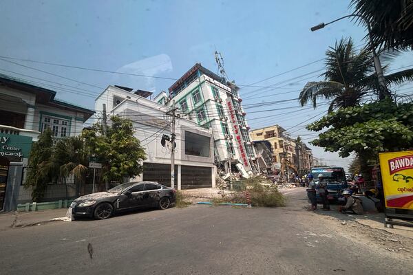 People stand near a damaged building in the aftermath of an earthquake, in Mandalay, central Myanmar, Sunday, March 30, 2025. (AP Photo/Thein Zaw)
