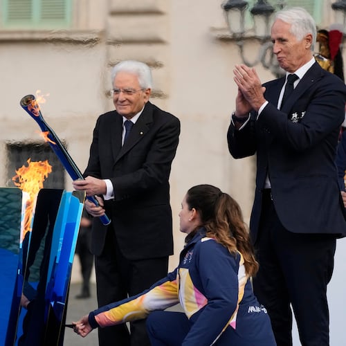 Italian President Sergio Mattarella holds the torch and lights the Milan Cortina 2026 Winter Olympics cauldron in front of the Quirinale Presidential Palace, in Rome, Friday Dec. 5, 2025. (AP Photo/Gregorio Borgia)