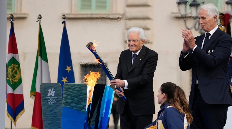 Italian President Sergio Mattarella holds the torch and lights the Milan Cortina 2026 Winter Olympics cauldron in front of the Quirinale Presidential Palace, in Rome, Friday Dec. 5, 2025. (AP Photo/Gregorio Borgia)