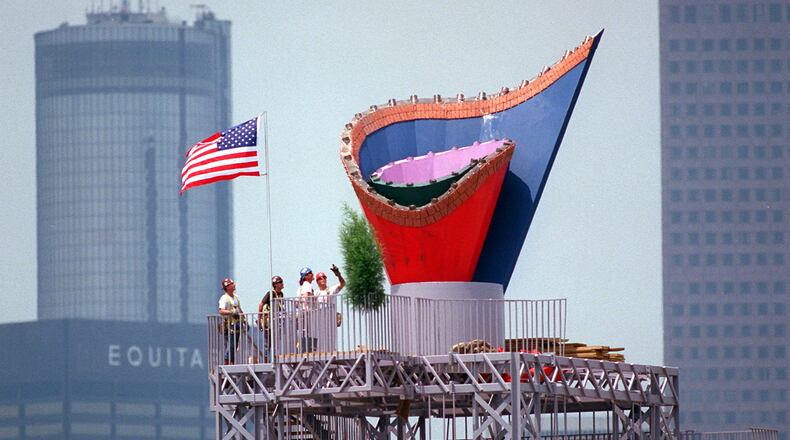 With a flag completing the picture, ironworkers admire their efforts after installing the Olympic Cauldron atop its 116-foot-high tower on May 30, 1996. The Cauldron, made of stainless steel, has a terra cotta rim of Georgia red clay. (Joey Ivansco/AJC 1996)