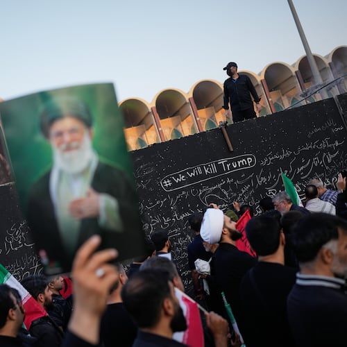 A mourner holds a portrait of the late Iranian Supreme Leader Ayatollah Ali Khamenei as he walks past a wall bearing messages, including one in English that reads "We will kill Trump," during the funeral ceremonies for Khamenei and members of his family at the Imam Khomeini Mosalla Grand Mosque in Tehran, Iran, Saturday, July 4, 2026. (AP Photo/Altaf Qadri)