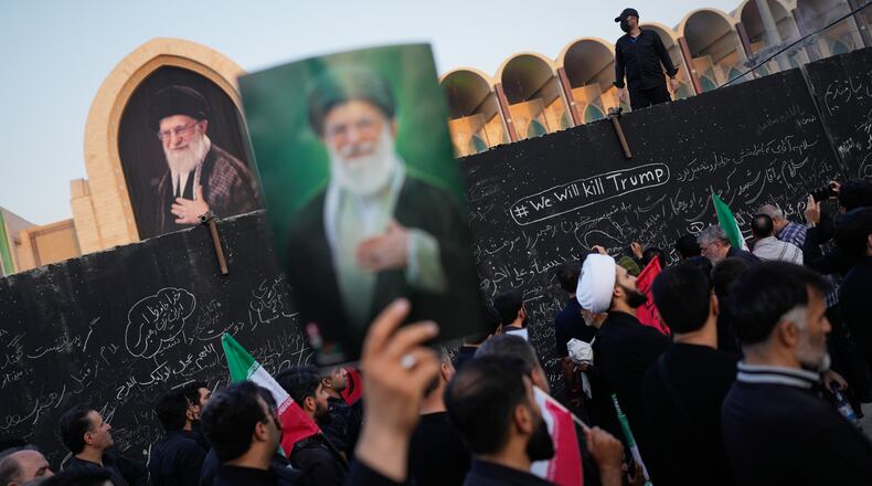 A mourner holds a portrait of the late Iranian Supreme Leader Ayatollah Ali Khamenei as he walks past a wall bearing messages, including one in English that reads "We will kill Trump," during the funeral ceremonies for Khamenei and members of his family at the Imam Khomeini Mosalla Grand Mosque in Tehran, Iran, Saturday, July 4, 2026. (AP Photo/Altaf Qadri)