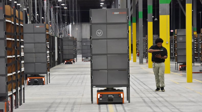 Isaac Jones of Project Verte monitors a warehouse robot in a training run as it moves a shelving unit to a station where a worker will remove ordered items. Robotics and artificial intelligence are quickly changing the warehouse business and jobs. Robots help the human get more done in shorter amounts of time. The upside is workers handle orders faster. The downside is fewer people are needed to get the work done than in less-automated warehouses. HYOSUB SHIN / HSHIN@AJC.COM