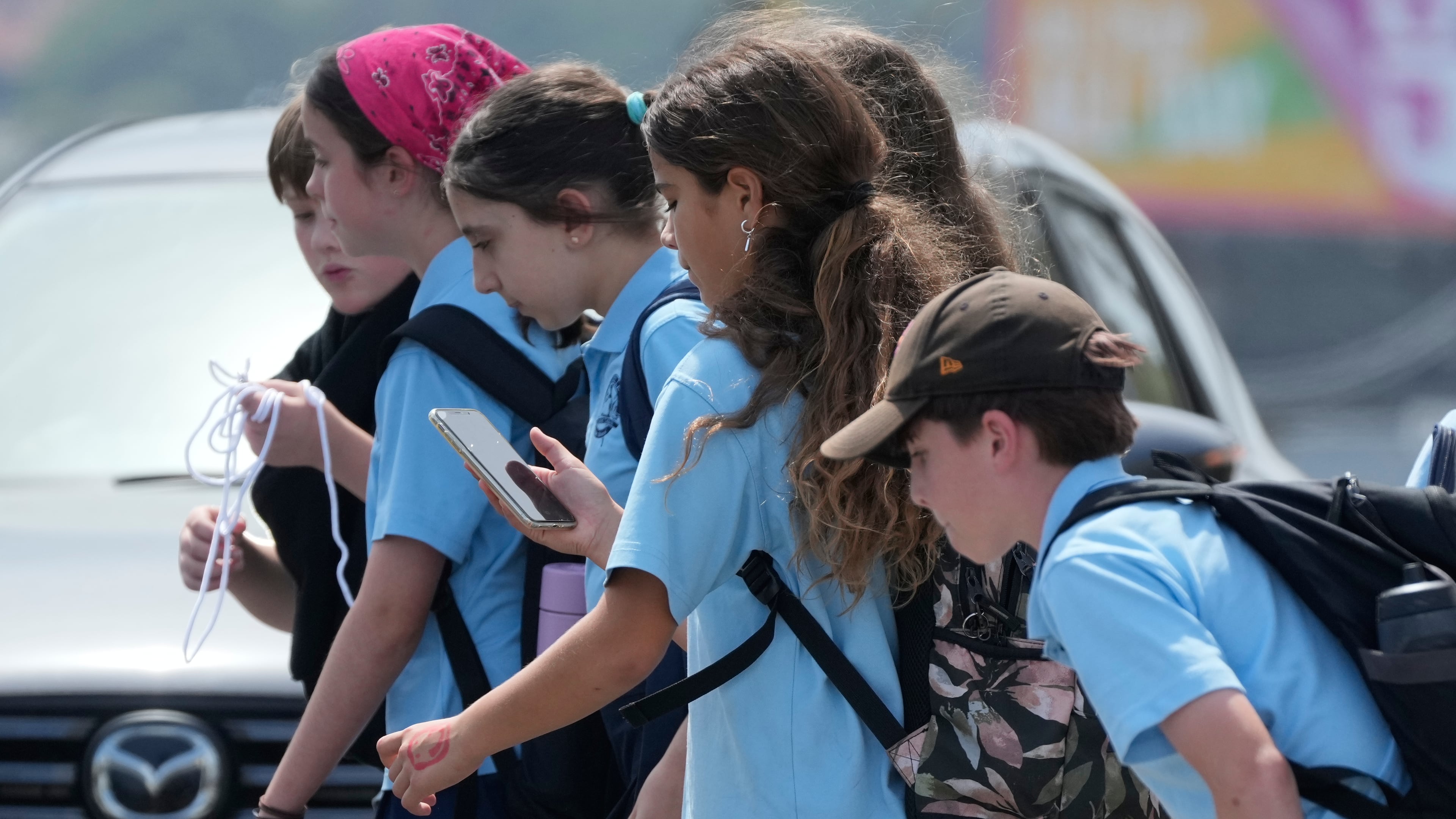 A school girl uses her phone as she walks with a group of kids in Sydney, Monday, Dec. 8, 2025. (AP Photo/Rick Rycroft)