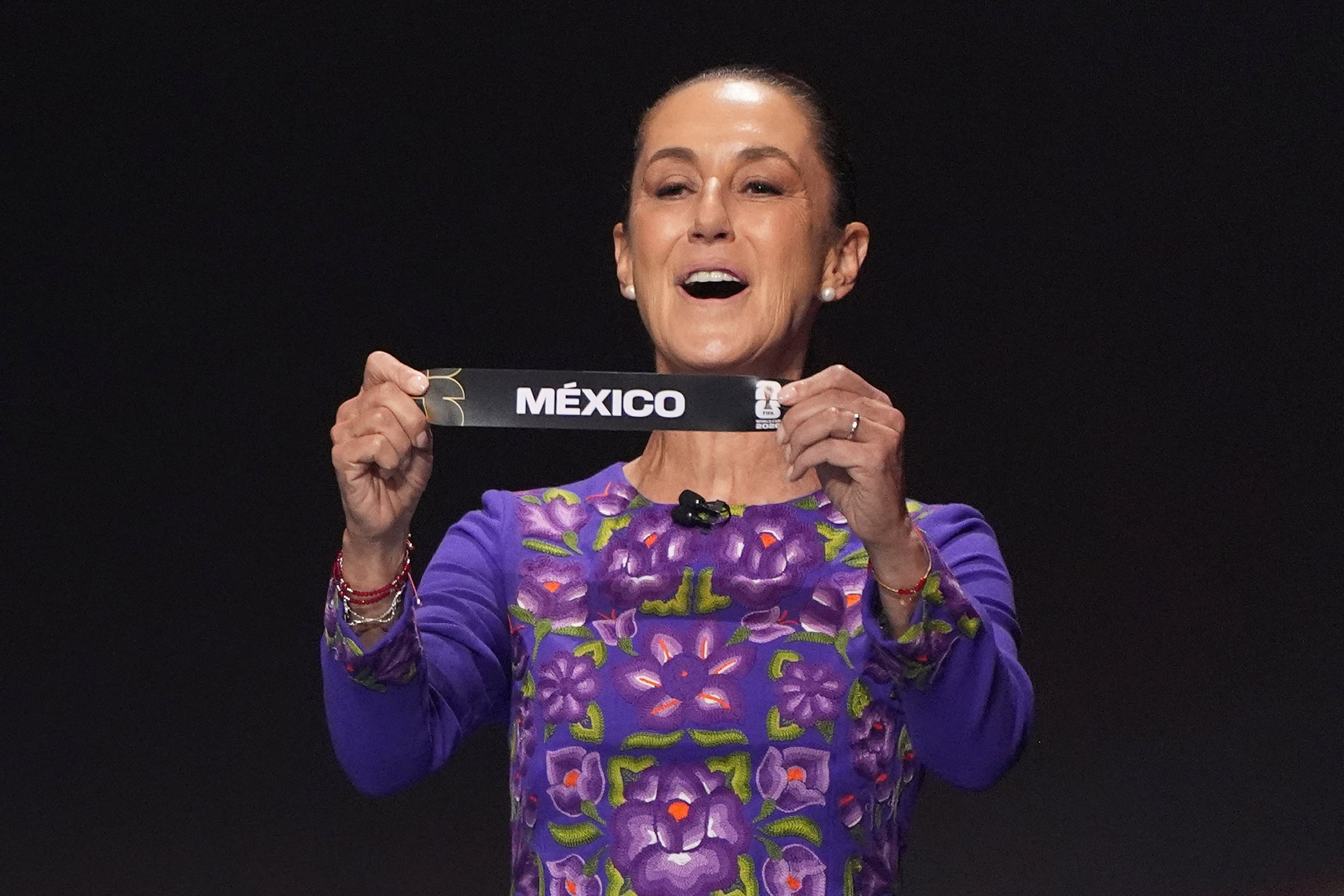 Mexican President Claudia Sheinbaum holds up the team name of Mexico during the draw for the 2026 soccer World Cup at the Kennedy Center in Washington, Friday, Dec. 5, 2025.(AP Photo/Evan Vucci)