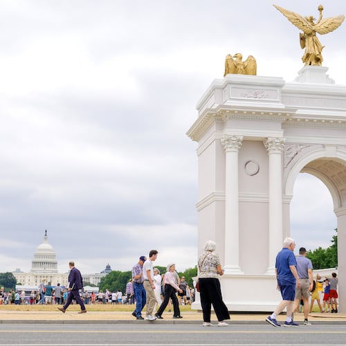 Visitors walk at the Great American State Fair with the triumphal arch model and the U.S. Capitol, in the background, Wednesday, July 8, 2026, in Washington. (AP Photo/Mariam Zuhaib)
