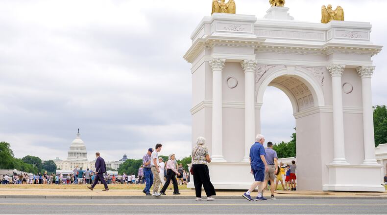 Visitors walk at the Great American State Fair with the triumphal arch model and the U.S. Capitol, in the background, Wednesday, July 8, 2026, in Washington. (AP Photo/Mariam Zuhaib)
