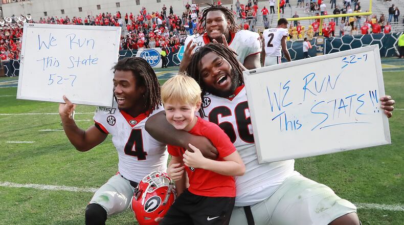 Georgia players James Cook ( left), Isaiah Wilson (top) and Solomon Kindley (right)  celebrate a 52-7 victory over Georgia Tech with head coach Kirby Smart's son Andrew in a NCAA college football game on Saturday, November 30, 2019, in Atlanta.  Curtis Compton/ccompton@ajc.com