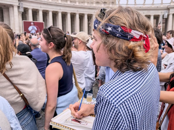 Notre Dame's architecture college student Wesley Buonerba, wearing a us flag bandanna, does a watercolor sketch of the loggia of St. Peter's Basilica during Pope Leo XIV first Sunday blessing of faithful gathered in the square for the traditional blessing, Sunday, May 11, 2025. (AP Photo/Giovanna Dell'Orto)