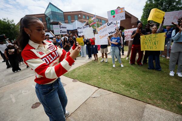 Student Kiara Huff takes a cellphone photo of fellow students as they protest outside the Morehouse School of Medicine on Wednesday, May 6, 2026. (Miguel Martinez/AJC)