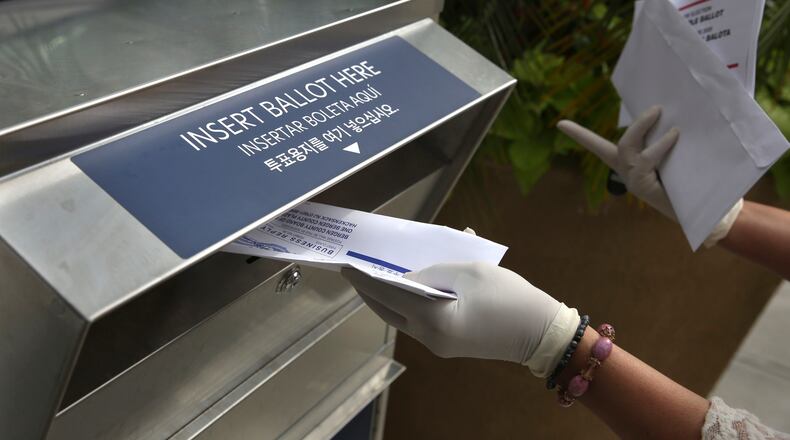 FILE - In this July 7, 2020, file photo a woman wearing gloves drops off a mail-in ballot at a drop box in Hackensack, N.J. (AP Photo/Seth Wenig, File)