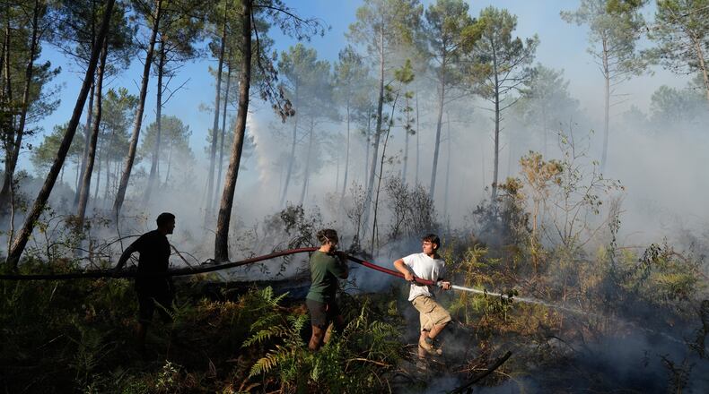 A group hold a firehose and try to suppress a fire near Lacanau, as wildfires rage outside Bordeaux, France, Monday, July 27, 2026. (AP Photo/Baz Ratner)