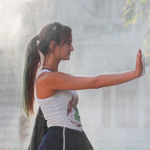 A woman pauses while she walks through a water mist machine installed by city administration to assist people in coping with the heat, as the National Weather forecaster issued an extreme heat code red warning for most parts of the country, in Bucharest, Romania, Thursday, Aug. 6, 2026. (AP Photo/Vadim Ghirda)