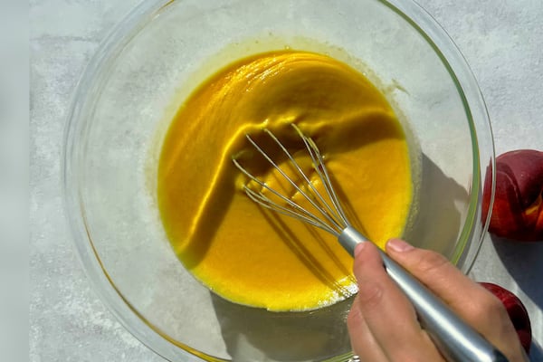 Hand whisks peach curd in a large glass bowl.